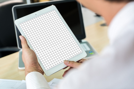 Close up the working man holding a Mock up and grid line on white tablet in hands, laptop and paper...