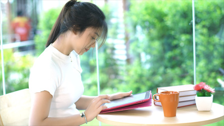 Asian teenage girl chatting or playing by tablet for relaxation, she sitting in garden zone and pile...