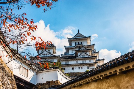 Beautiful landscape from white outer wall and Japanese Castle with sunlight and foreground the branch of red maple tree with blue sky backgroundのeditorial素材