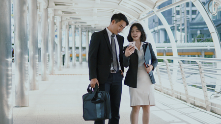 The pretty woman show map in her smartphone to young businessman hold briefcase, blurred modern building  background の写真素材