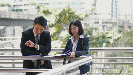 Close up the handsome businessman looking at wristwatch and pretty woman view the documents in the file,  co-worker conceptの写真素材