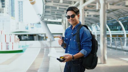 Portrait Asian Handsome young man wearing a shirt jeans and sunglasses holding paper map and smartphone in left hand and thump up the right hand and smile to camera, copy spaceの写真素材