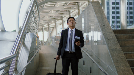 Asian young businessman walks along the tow bag with haste, and reading the signpostの写真素材