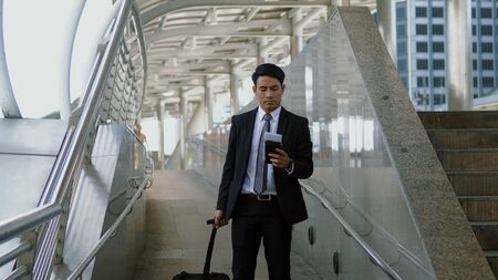 Asian young businessman walks along the baggage with haste, and reading the paper map in handの写真素材