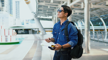 Portrait Asian Handsome young man wearing a shirt jeans and sunglasses holding paper map and smartphone in left hand and thump up the right hand and look forward, copy spaceの写真素材