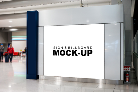 Mock up large blank advertising billboard on the glass panel inside airport terminal with clipping path, nearly waiting seat and blurry people backgroundの写真素材