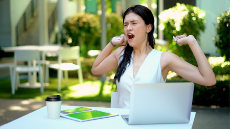 The pretty woman yawned and stretched, On her desk has equipment technology with smartphone, tablet and laptop computer to workの写真素材