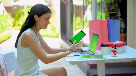 The beautiful business woman used technology equipment with green screen for working, Holding smartphone in her hand, typing on laptop and tablet placed on tableの写真素材