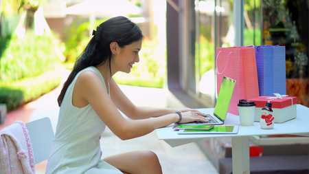 The pretty woman looking at laptop with cheerful, she smile and typing on keyboard of laptop, has tablet, smartphone with green screen and shopping bag nearlyの写真素材
