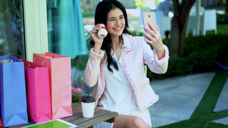 The pretty woman use video call to showing a lovely santa doll in her hand with smartphone and many shopping bag nearlyの写真素材