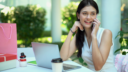 Close up the young pretty business woman talking to smartphone and looking forward while use laptop for working in gardenの写真素材