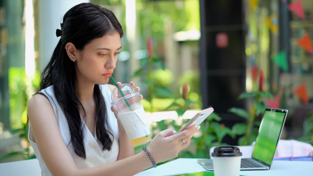Close up the beautiful woman feel frustrated while using a smartphone and holding a beverage glass in her handの写真素材