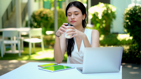Close up the young woman pick up a coffee cup on table in garden, has laptop, smartphone, tablet  with green screen placed nearlyの写真素材