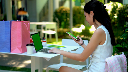 The pretty woman looking to laptop with cheerful, she a handful and smile as the winner, has tablet with green screen and shopping bag nearlyの写真素材