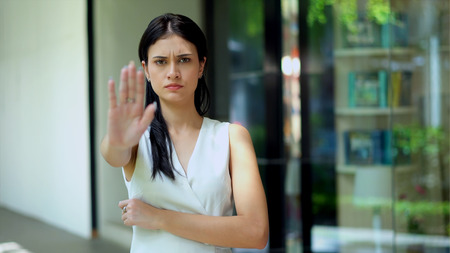 The young woman standing with hugging chest looking camera and she lifted the hand for stop and serious actionの写真素材