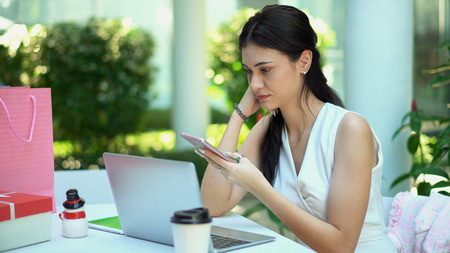Close up the pretty woman looking smartphone in her hand, has laptop and tablet placed on tableの写真素材