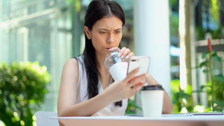 Close up the young pretty woman frustrated  and bored while using smartphone and sucking cold coffee from a tube with boringの写真素材