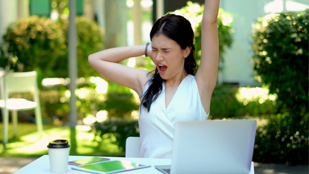 The pretty woman yawned and stretched, On her desk has equipment technology with smartphone, tablet and laptop computer with green screen to workの写真素材