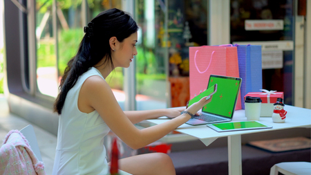 The beautiful business woman used technology equipment with green screen for working, Holding smartphone in her hand, typing on laptop and tablet placed on the deskの写真素材