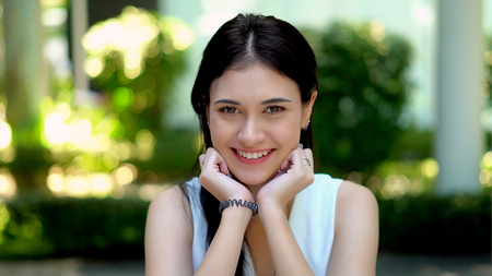 Close up portrait a lovely young woman is sitting and put the chin on hands and smiling to cameraの写真素材