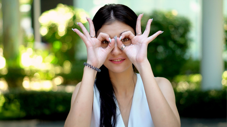 Close up portrait a pretty young woman smiling and show two hands with sign ok on her eyes to cameraの写真素材