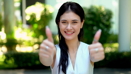 Close up and selective focus at a lovely young woman has big smiling and blurred two hands with thumbs up to cameraの写真素材