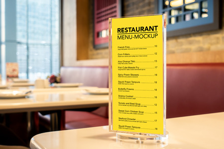 Mock up vertical blank signboard or menu with clipping path in acrylic stand on table in the restaurant, yellow screen empty space for promotion or information food items with blurred backgroundの写真素材