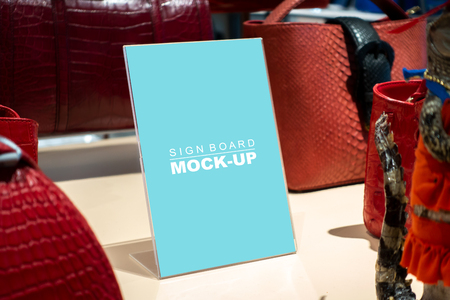 Mock up vertical blank signboard with clipping path in acrylic stand on table to show price or promotion beautiful bag, blue screen empty space for promotion or advertising in fashion shopの写真素材