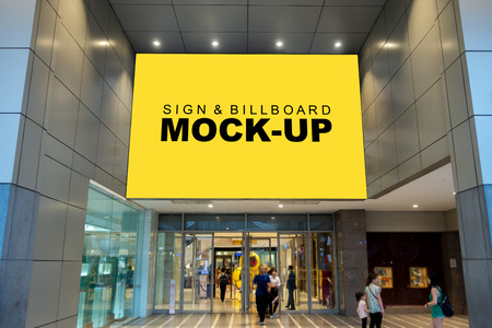 Mock up large billboard with clipping path on the wall over the entrance shopping mall, perspective yellow screen empty space to insert advertisement, blurred people walking in and out the doorの写真素材