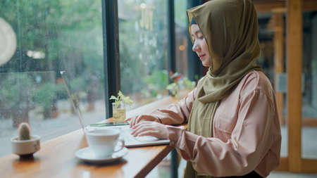Young pretty muslim woman wearing hijab and use laptop for working at coffee shop, startup business woman working out the office, copy spaceの写真素材