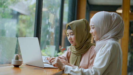 Selective focus, Two beautiful Muslim women are working on laptop computer, They looking on screen and discussing in a coffee shop, muslim business working concept, copy spaceの写真素材