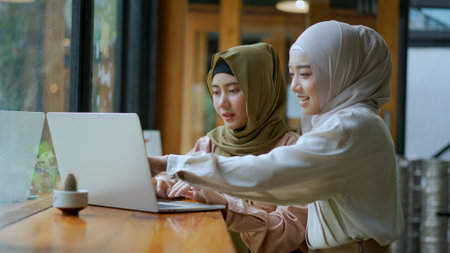 Selective focus, Two beautiful Muslim women are working on laptop computer and discussing in a coffee shop, muslim business working conceptの写真素材
