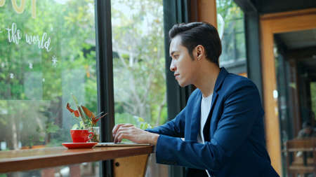 Young  man in blue formal suit sitting and typing on laptop computer for work or checking E-mail  while working outside office,  copy spaceの写真素材