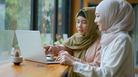 Selective focus, Two beautiful Muslim women are working on laptop computer, They looking on screen and discussing in a coffee shop, muslim business working concept, copy spaceの写真素材