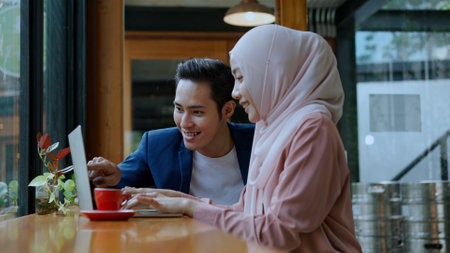 Selective focus, Young muslim woman wearing hijab and young man friend working on laptop, They use laptop computer in coffee shop, muslim business working conceptの写真素材