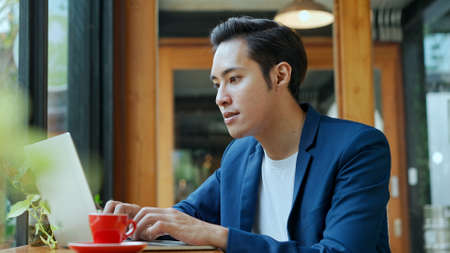 Portrait Young  man in blue formal suit sitting and typing on laptop computer for work or checking E-mail  while working outside office,  copy spaceの写真素材