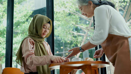 selective focus, Young beautiful muslim woman wearing hijab sitting near glass window in coffee shop payment with credit card  to senior waitressの写真素材