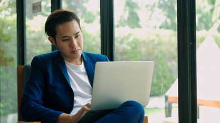 Handheld shot, young handsome muslim man sitting in coffee shop, he smiling during use laptop to working  with happinessの写真素材