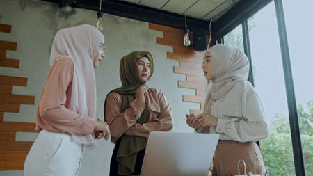 Young beautiful muslim women wearing hijab and use laptop while brainstorm meeting, they are talking together in meeting roomの写真素材