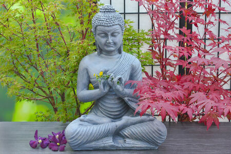 buddha statue with flower decorations and maple treesの写真素材