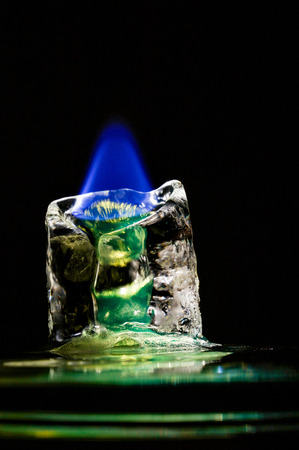 Blue flame melting down greenish icecube in front of black backgroundの写真素材