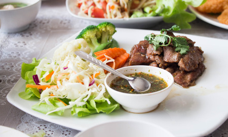 grilled pork with fresh vegetable and thai spicy suace on white plateの写真素材