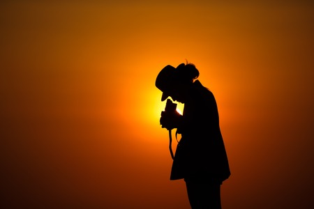 Silhouette of woman shooting with camera at sunset