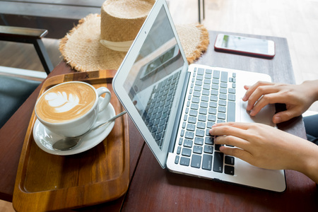 Women's hands typing on computer with coffee and smart phone