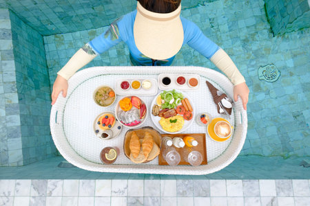 young asian woman  with breakfast floating on swimming pool in hotelの写真素材