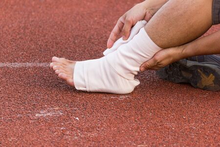 Male athlete applying compression bandage onto ankle injury of a football player, Sports injuries.の写真素材