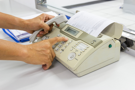 Hand man are using a fax machine send paper in the office Business conceptの写真素材