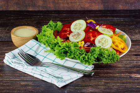Close up A green salad is a dish of a mixture of small vegetables, Cucumbers fragrant vegetables tomatoes peppers corn carrots on wood table.の写真素材