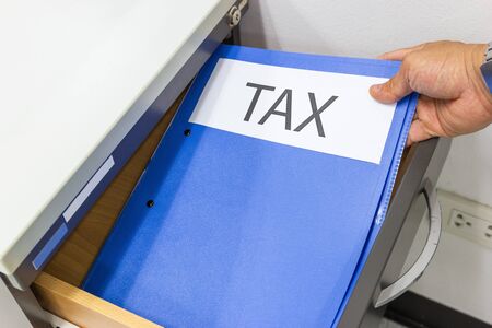 Hand of Man hold Tax Files folder in the file cabinetの写真素材