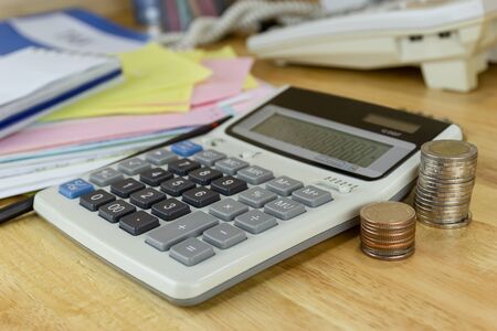 the stack of coin with calculator on wood table at office, concept of calculating expenses, incomes and expenses.の写真素材